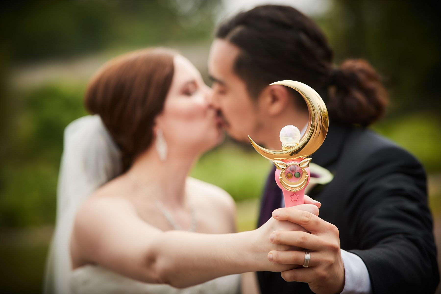 a bride and groom kiss while holding the moon stick up to the camera