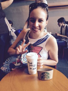 A young white woman does the peace sign while her starbucks cup reads "Thank you so cute!!"