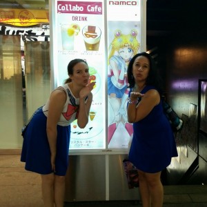 Two young women stand inf front of the Sailor Moon cafe, blowing kisses like Sailor Moon