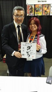 A young woman and Akira Takarada pose for a picture, holding a sign that says Godzilla in katakana