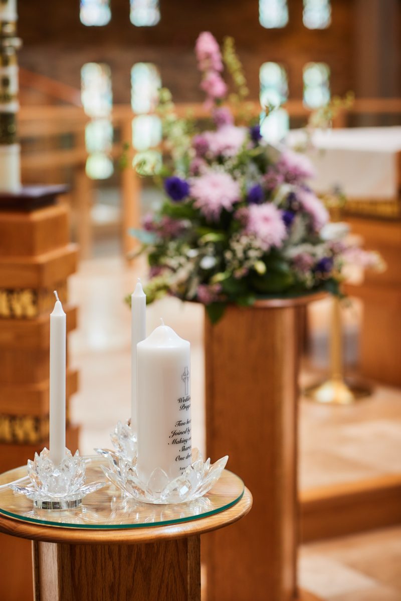 a unit candle and two taper candles sit in crystal lotus holders with purple flowers in the background